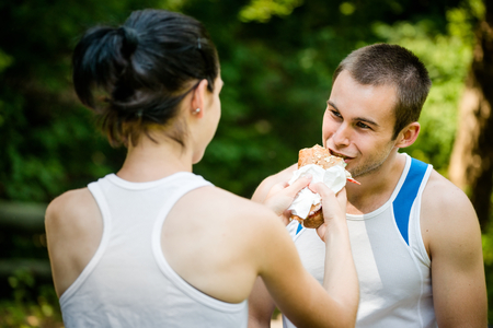 Young couple eating after sport training outdoor in nature - woman feeds manの写真素材