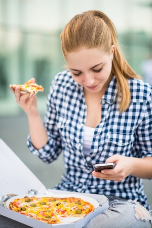 Teenager eating pizza looking in phoneの写真素材