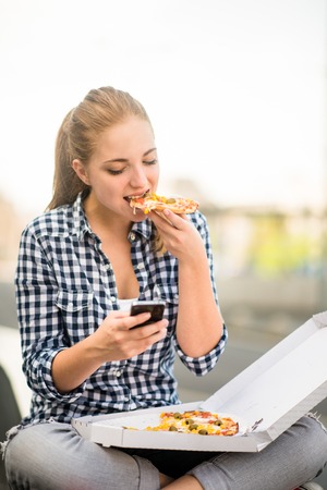 Teenager eating pizza looking in phoneの写真素材