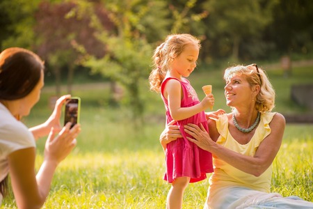 Mother taking photo of her child with grandmother eating icecream outdoor in parkの写真素材