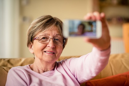 Close-up of senior woman taking selfie with mobile phone at homeの写真素材