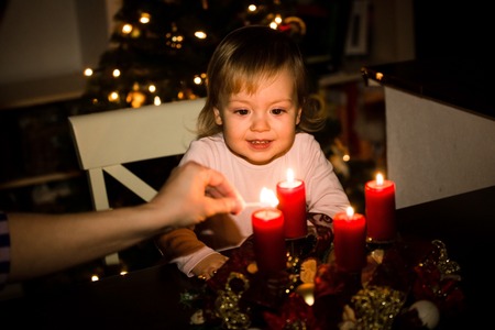 Child watching lighting of advent wreath with red candles, christmas tree in backgroundの写真素材