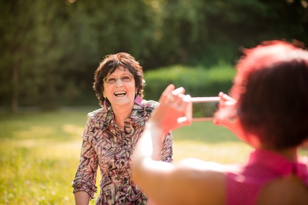 Woman is photographing her senior mother with mobile phone outdoor in nature