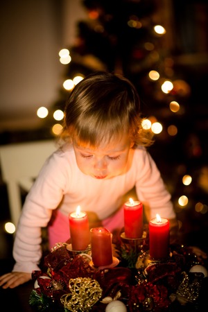Little child blowing candles on advent wreath, christmas tree in backgroundの写真素材