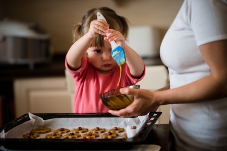 Child baking cookies together with her mother - painting honey cakes with egg yolk