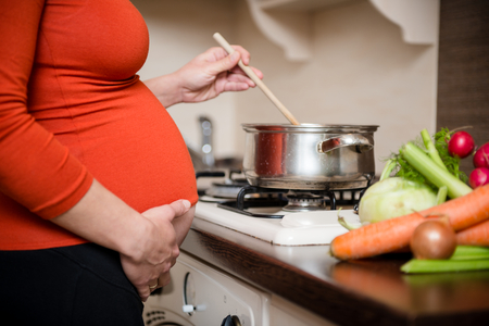 Crop of belly - pregnant woman cooking vegetables in kitchenの写真素材