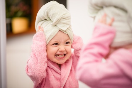 Little child having fun in front of big mirror after bath with towel on headの写真素材