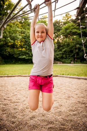 Outdoor portrait of girl hanging from playground net