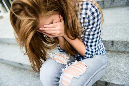 Unhappy depressed teenager with face in hands sitting outdoorの写真素材