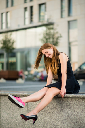 Which shoes to choose - teenager on street one foot in sneaker and other in high heelの写真素材