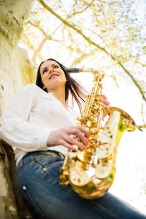Young beautiful saxophonist with saxophone - outdoor in natureの写真素材