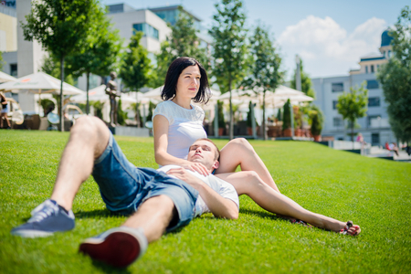 Young couple date - woman sitting on grass with his head laid on her tightsの写真素材