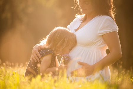 Little child kissing belly of her mother outdoor in sunny natureの写真素材