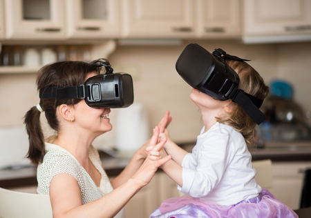 Mother and child playing together with virtual reality headsets indoors at homeの写真素材