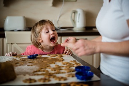 Mother giving her daughter to taste piece of doughの写真素材