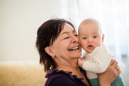 Senior woman hugging with her baby grandchild - interior sceneの写真素材