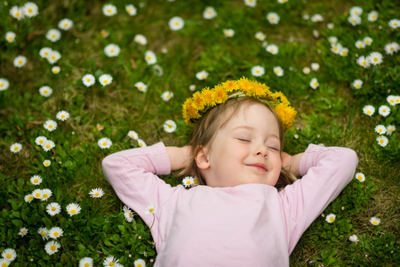 Little girl with dandelion wreath on head lying in grass full of daisy flowers - above viewの写真素材