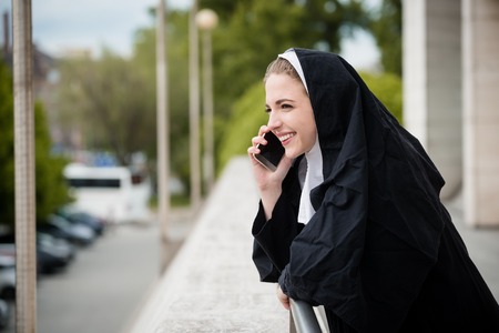 Young nun in black dress calls phone - outdoors settingの写真素材