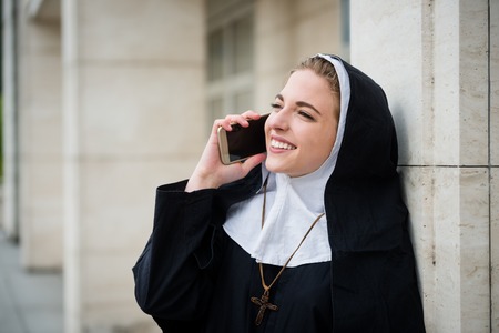 Young catholic nun calling phone - ouutside leaning at buildingの写真素材