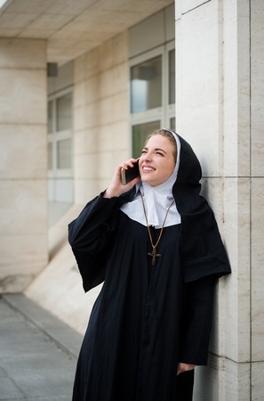 Young catholic nun calling phone - ouutside leaning at buildingの写真素材