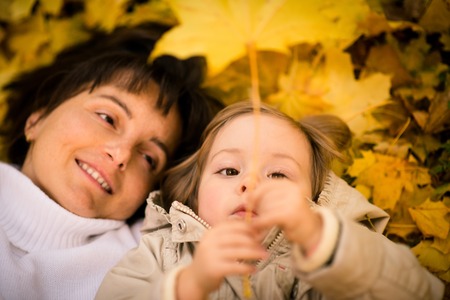 Mother and daughter playing with leaf - lying on ground full of autumn fallen leavesの写真素材