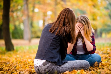 Friends talk outside in autumn nature - one girl is caressing and listening to another teenage girl with problemsの写真素材