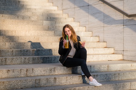 Teen girl eating sandwich and drinking juice outdoor sitting on stairsの写真素材