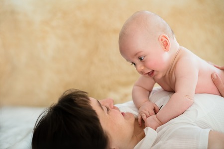 Mother playing with her little baby boy on sofu at homeの写真素材