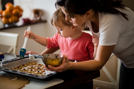 Mother and child baking together - child spreading yolk on honey cakesの写真素材