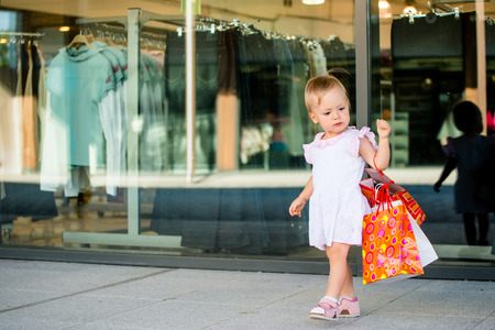 Cute baby goes shopping with bags, shops in backgroundの写真素材