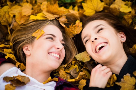 Two friends lying on ground in fallen leaves and having fun in autumnの写真素材