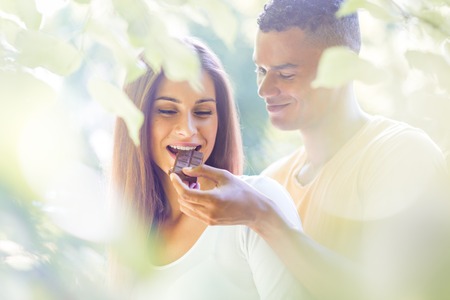 Young man feeding her girl with chocolate outdoor in nature - soft toneの写真素材