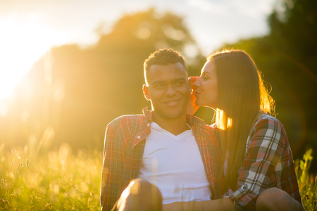 Young woman whispering to man - outdoor in nature with setting sun in backgroundの写真素材