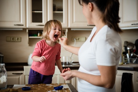Mother giving her daughter to taste piece of doughの写真素材