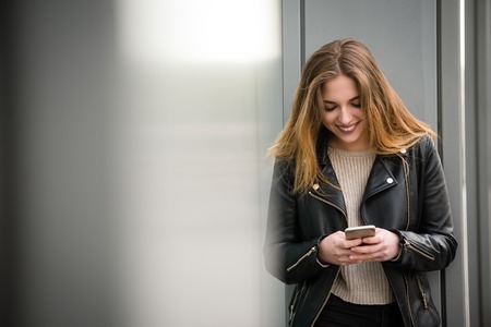 Young modern woman communicating with friends through social media on phone outdoor in street