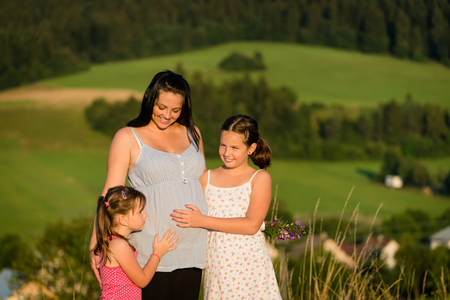 Pregnant loving mother with her adorable daughtersの写真素材