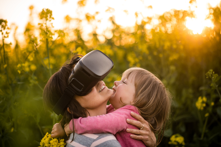 Mother uses head-mounted display in rapeseed field while hugging girl child.の写真素材