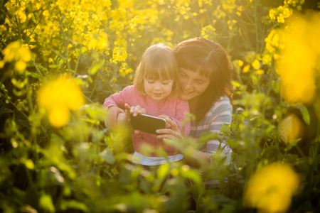 Happy cute daughter and mother on yellow field flowersの写真素材