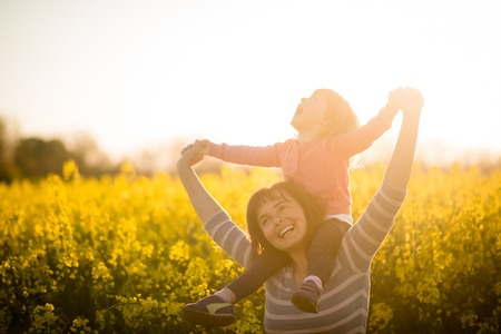Cute joyous kid girl riding on shoulders of her motherの写真素材