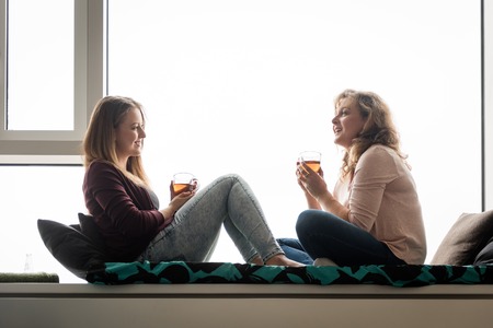 Women having tea at home on window ledge bedの写真素材