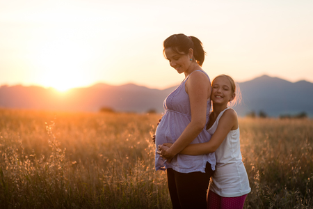 Daughter hugging her pregnant mother from behindの写真素材