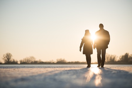 Couple walking through frozen lake as sun setsの写真素材