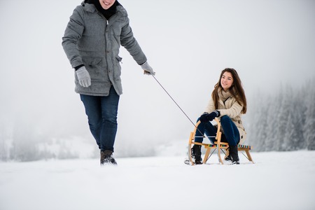 Man pulling woman on sleigh in winter forestの写真素材