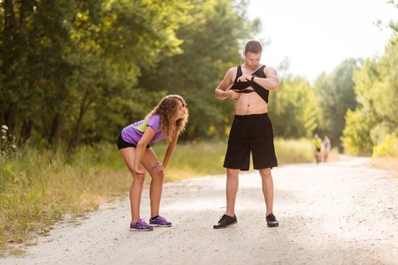 Guy monitoring his heart rate as tired woman takes a break from runningの写真素材