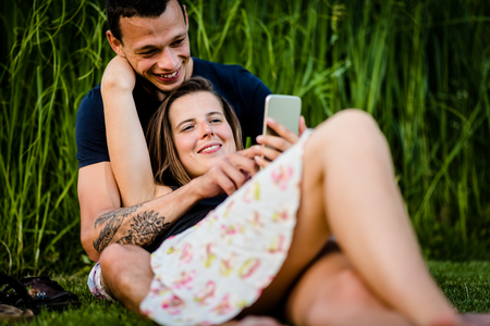Playful couple smiling while using smartphoneの写真素材