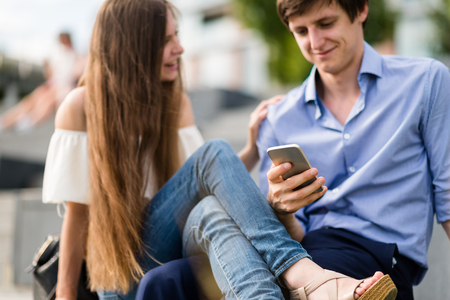 Couple sitting together while man using phoneの写真素材
