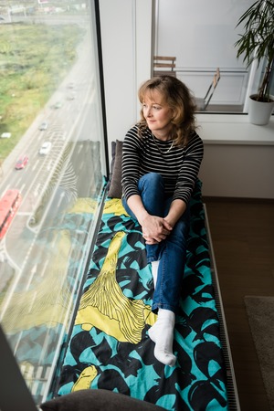 Woman sitting on the window ledge bedの写真素材