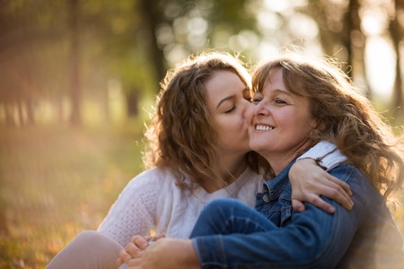 Senior woman is kissed by her adult daughterの写真素材