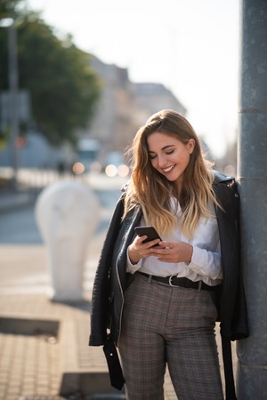 Woman with smartphone leaning against light postの写真素材