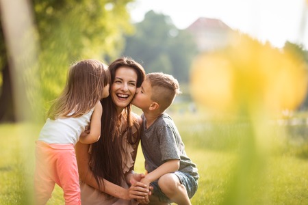 Siblings kissing their mother on her cheeksの写真素材
